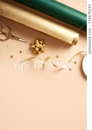 Green and brown wrapping paper rolls, scissors, and gold stars on beige background. Copy space for holiday text or design. 136676244