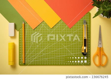 Colorful flat lay of crafting and stationery tools with cutting mat, scissors, knife, pencil, glue and paper sheets. Copy space Colorful flat lay of crafting and stationery tools with cutting mat, scissors, knife, pencil, glue and paper sheets. Copy space 136676245