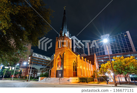 St. Peter's Co-Cathedral in Jackson Mississippi. Historic Gothic Revival Catholic architecture features a brick facade and tall central spire illuminated at night 136677131