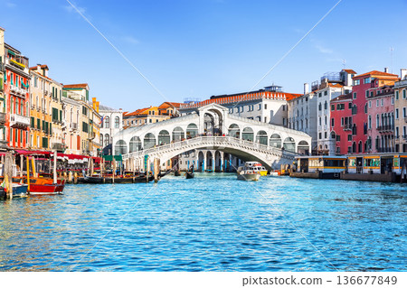 Famous Rialto Bridge spanning the Grand Canal in Venice, Italy, surrounded by historic colorful buildings and turquoise water under clear blue sky. Famous Rialto Bridge spanning the Grand Canal in Venice, Italy, surrounded by historic colorful buildings and turquoise water under clear blue sky. 136677849