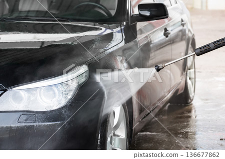 A man washes his car at a self service car wash. The car is washed using high pressure water. Self-service car wash. A man washes his car at a self service car wash. The car is washed using high pressure water. Self-service car wash. 136677862