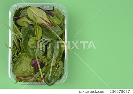 Mixed baby salad leaves in plastic container on green background 136678027