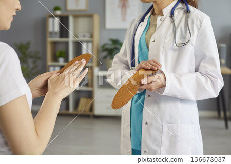 Orthopedic surgeon, orthopedist medical professional showing shoe insoles to patient in clinic  136678087