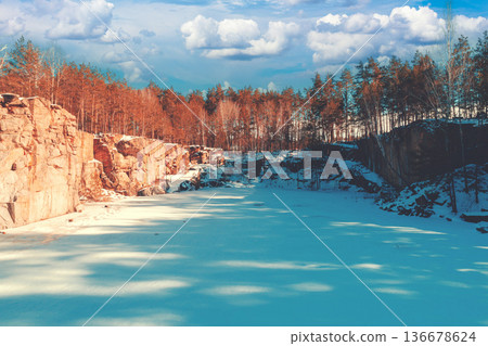 Winter nature. Frozen lake with a rocky shore. Granite quarry on a sunny day Winter nature. Frozen lake with a rocky shore. Granite quarry on a sunny day 136678624