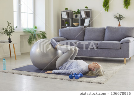 Healthy sport exercise with fitness ball of senior woman, lying on home floor with feet on ball Healthy sport exercise with fitness ball of senior woman, lying on home floor with feet on ball 136678956