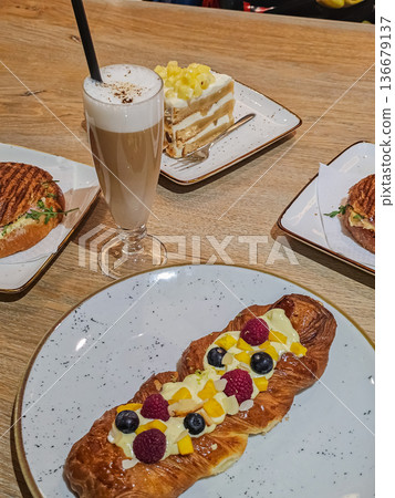 Side View of Latte Coffee with Pineapple Roll, Berry Tart and Ham Sandwich Side View of Latte Coffee with Pineapple Roll, Berry Tart and Ham Sandwich 136679137