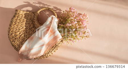 Woven Straw Handbag with Silky Scarf and Flowers. Elegant Summer Fashion Flatlay on Peach Background Woven Straw Handbag with Silky Scarf and Flowers. Elegant Summer Fashion Flatlay on Peach Background 136679314