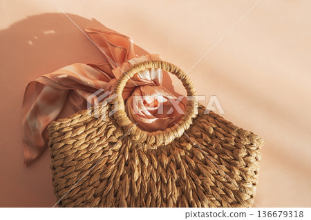 Woven Straw Handbag with Silky Scarf. Elegant Summer Fashion Flatlay on Peach Background 136679318