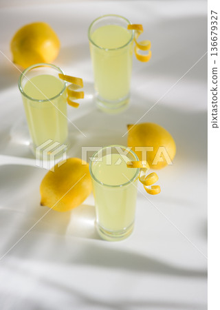 Limoncello Glasses with Curled Lemon Peels and Fresh Lemons. Refreshing Summer Italian Beverage 136679327