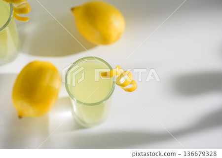 Limoncello Glasses with Curled Lemon Peels and Fresh Lemons. Refreshing Summer Italian Beverage 136679328