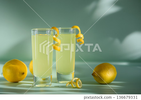Limoncello Glasses with Curled Lemon Peels and Fresh Lemons  on Light Green Background. Refreshing Summer Italian Beverage 136679331