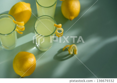 Limoncello Glasses with Curled Lemon Peels and Fresh Lemons  on Light Green Background. Refreshing Summer Italian Beverage 136679332