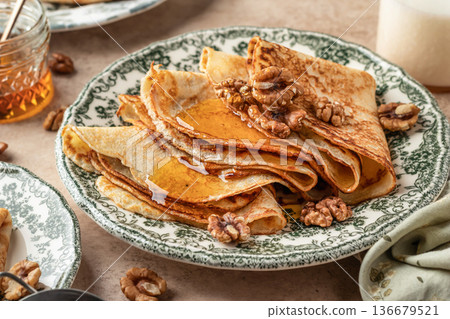Delicious crepes served with nuts and honey folded on ceramic plate close up. Tasty morning breakfast on beige table background, Maslenitsa concept Delicious crepes served with nuts and honey folded on ceramic plate close up. Tasty morning breakfast on beige table background, Maslenitsa concept 136679521