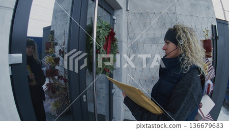 Professional Female Courier Hands Over Large Document Envelope to Man at Front Door Professional Female Courier Hands Over Large Document Envelope to Man at Front Door 136679683