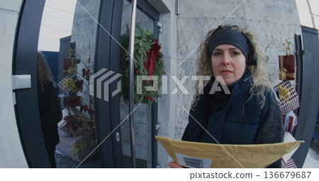 Professional Female Courier Hands Over Large Document Envelope to Man at Front Door Professional Female Courier Hands Over Large Document Envelope to Man at Front Door 136679687