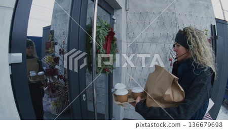 Female Courier With Headset Delivers Hot Coffee Cups and Brown Paper Bag to Man Doorstep 136679698