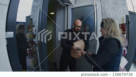 Courier Takes Bag and Hands to Customer, Who Pays Contactless Using Smartphone Courier Takes Bag and Hands to Customer, Who Pays Contactless Using Smartphone 136679736