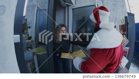 Postal Courier Dressed in Santa Costume Delivers Envelope Woman at Doorstep Postal Courier Dressed in Santa Costume Delivers Envelope Woman at Doorstep 136679749