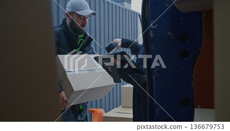 Man Moves Parcels From Pallet Jack Into Blue Van While Woman Scans Barcodes and Checks Tablet 136679753