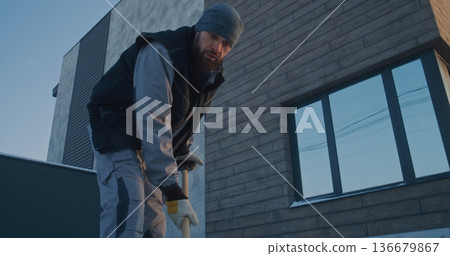 Focused Man Shoveling Snow Near Modern Residential House in Winter Focused Man Shoveling Snow Near Modern Residential House in Winter 136679867