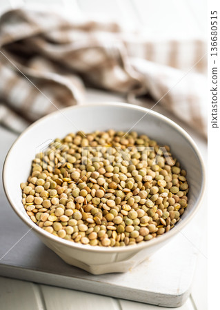 Uncooked green lentil in bowl on white table. Uncooked green lentil in bowl on white table. 136680515