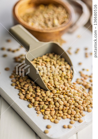 Uncooked green lentil in scoop on white table. Uncooked green lentil in scoop on white table. 136680516