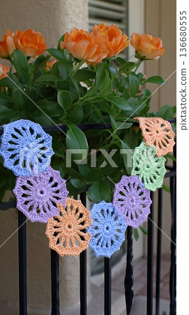 Crochet Garland Displays Colorful Flowers Near Blooming Roses on a Sunny Day Outdoors 136680555