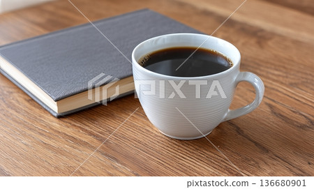 Coffee Cup Sits Next to a Closed Notebook on a Wooden Table During a Quiet Morning Coffee Cup Sits Next to a Closed Notebook on a Wooden Table During a Quiet Morning 136680901