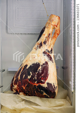 Raw beef carcass hanging on hook in refrigerated meat storage chamber, frost on walls. Concept of meat processing, meat production, butcher industry supply chain, meat curing, charcuterie industry Raw beef carcass hanging on hook in refrigerated meat storage chamber, frost on walls. Concept of meat processing, meat production, butcher industry supply chain, meat curing, charcuterie industry 136681071