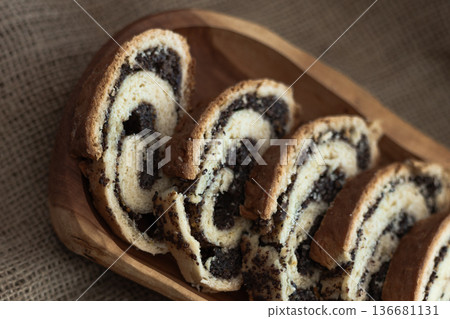 Rustic presentation of sliced poppy seed roll on a wooden serving board with burlap cloth underneath Rustic presentation of sliced poppy seed roll on a wooden serving board with burlap cloth underneath 136681131