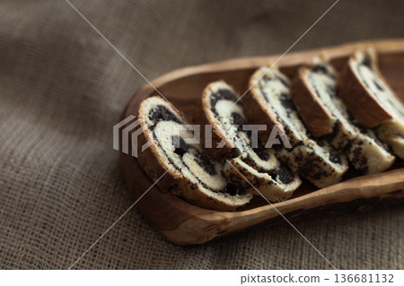 Close up of homemade poppy seed roll slices displayed on a long wooden platter over burlap surface Close up of homemade poppy seed roll slices displayed on a long wooden platter over burlap surface 136681132