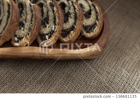 Classic poppy seed roulade sliced and served on rustic wooden plate over textured linen surface Classic poppy seed roulade sliced and served on rustic wooden plate over textured linen surface 136681135