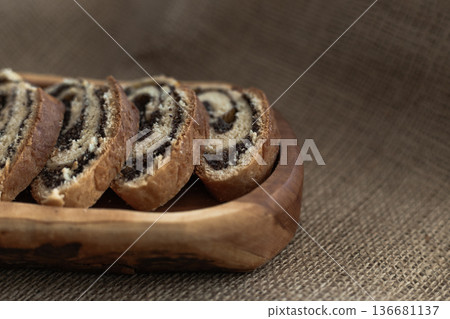 Fresh slices of traditional poppy seed bread roll presented on wooden board with rustic textile background 136681137