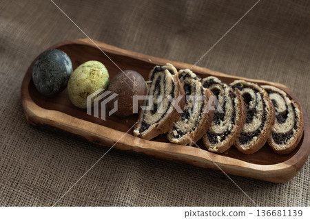 Traditional Easter composition with sliced poppy seed roulade and three dyed eggs on wooden serving board Traditional Easter composition with sliced poppy seed roulade and three dyed eggs on wooden serving board 136681139