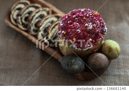 Easter still life with sliced poppy seed roll, three dyed eggs and traditional Easter cake on a wooden plate, rustic festive setting Easter still life with sliced poppy seed roll, three dyed eggs and traditional Easter cake on a wooden plate, rustic festive setting 136681140