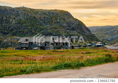 Weathered wooden houses in Teriberka at dusk, Russia, Kola Peninsula, evoke a bygone era, standing as silent witnesses to the passage of time. Teriberka's historical architecture concept 136681780
