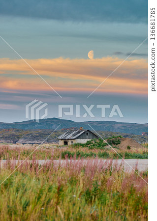 Weathered wooden houses in Teriberka at dusk, Russia, Kola Peninsula, evoke a bygone era, standing as silent witnesses to the passage of time. Teriberka's historical architecture concept 136681785