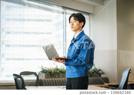 一位身穿工作服的年輕男子正在使用筆記型電腦 一位身穿工作服的年輕男子正在使用筆記型電腦 136682160