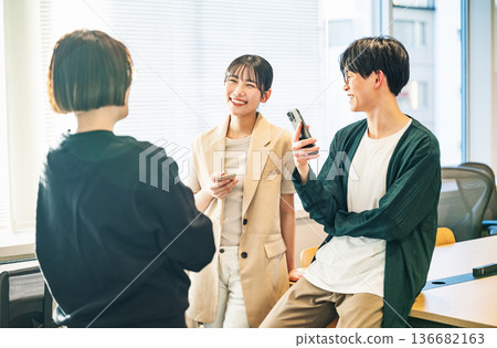 年輕男女一邊聊天一邊拿著智慧型手機 136682163