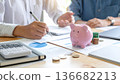 Close up of a pink piggy bank on a desk with people calculating budget and financial planning charts. 136682213