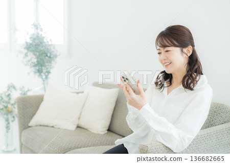 一個女人在客廳裡看著她的智能手機 一個女人在客廳裡看著她的智能手機 136682665