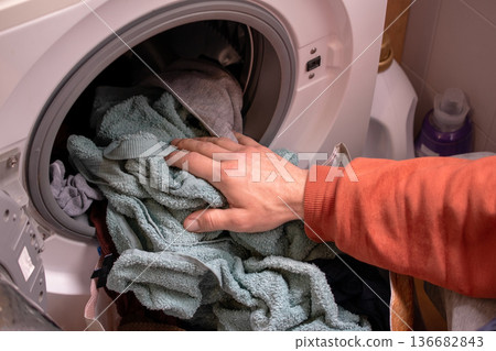 Hand putting clothes into a front-loading washing machine Hand putting clothes into a front-loading washing machine 136682843