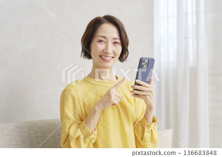 Woman using smartphone in living room, portrait, looking at camera 136683848