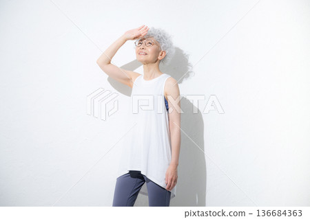 A cheerful, gray-haired senior woman in sleeveless sportswear looking up, full body A cheerful, gray-haired senior woman in sleeveless sportswear looking up, full body 136684363