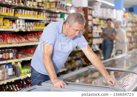 Mature man shopping in supermarket, choosing frozen convenience food Mature man shopping in supermarket, choosing frozen convenience food 136684723