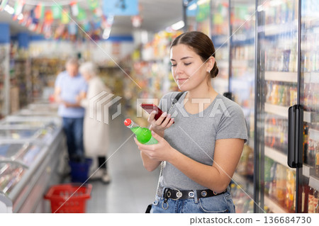 Woman purchaser scanning label of cool drink by phone Woman purchaser scanning label of cool drink by phone 136684730