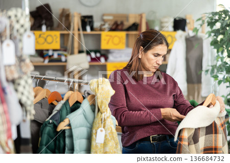 Adult woman chooses plaid jacket in clothing store 136684732