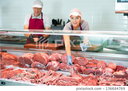 Positive young saleswoman vendor in apron and disposable gloves shows meat tenderloin 136684769