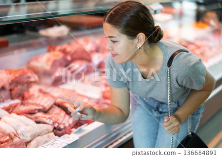 Young girl choosing fresh raw meat in display case in butcher shop 136684891