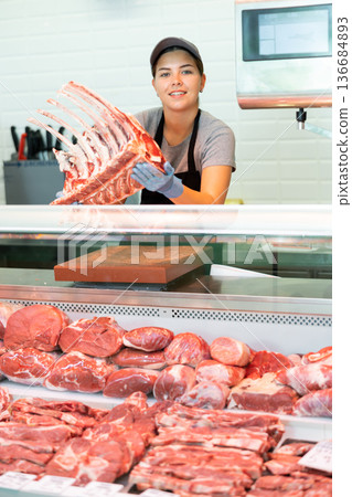 Sales assistant girl shows beef flat ribs in butcher shop Sales assistant girl shows beef flat ribs in butcher shop 136684893